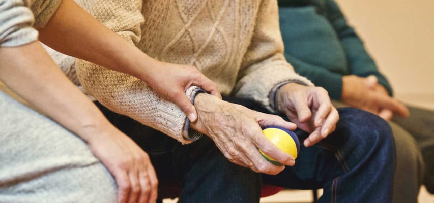 An older adult holding a ball with staff support