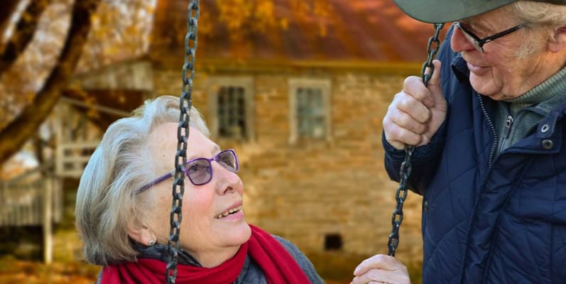 Elderly couple smiling while on a swing in a park