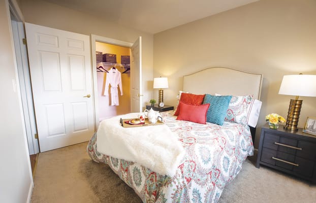 A stylish bedroom featuring a bed with colorful pillows, a bedside table, and a walk-in closet.