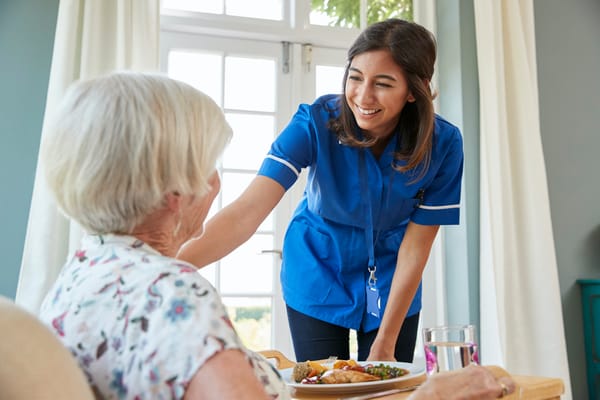 Staff member serving food to a resident in a cozy room