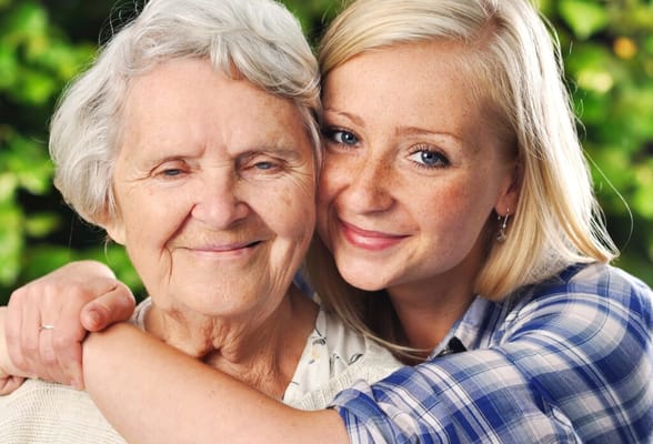 An elderly woman and a young woman smiling together in a garden