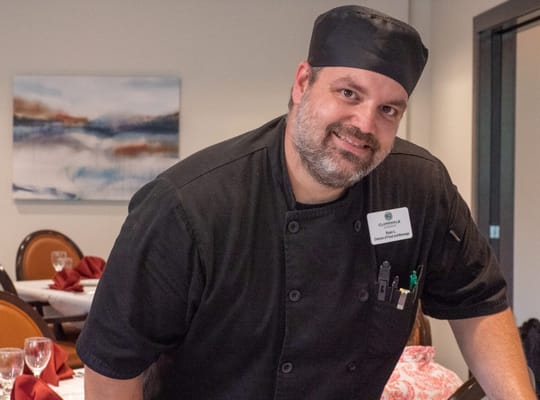 Chef serving in the dining area with beautifully set tables