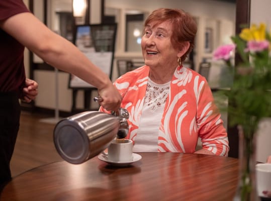 Woman enjoying coffee served by staff in a common area
