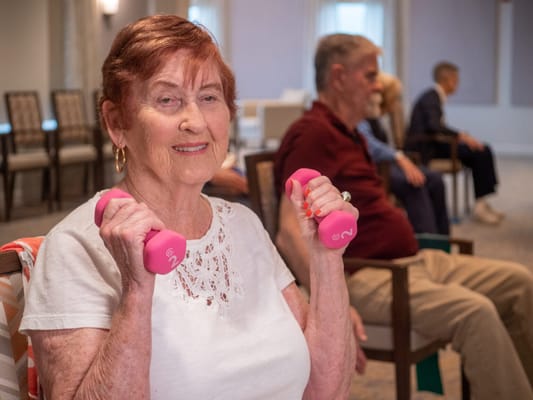 An elderly woman holding pink dumbbells in an activity room