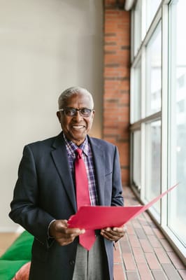 Smiling senior man holding a red folder by a window
