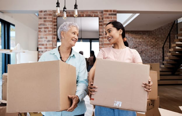 Two women in an interior space carrying boxes