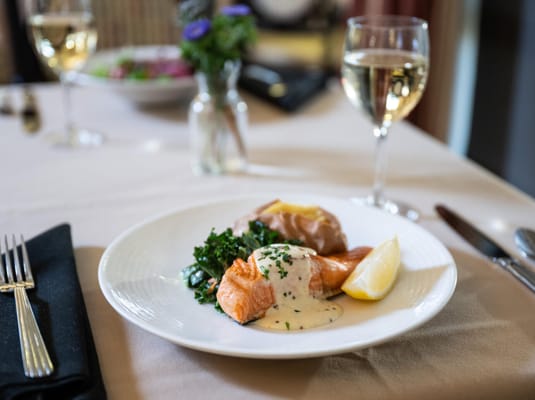 A plated meal featuring salmon, greens, and a glass of wine