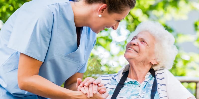 Staff member holding hands with a smiling resident outdoors