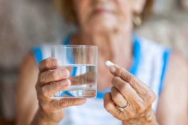 An elderly woman holding a glass of water and a pill
