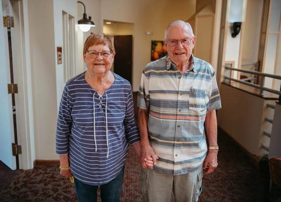Two residents smiling and holding hands in a hallway