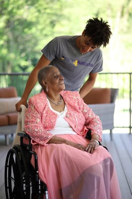 A resident smiling in a wheelchair with staff assistance