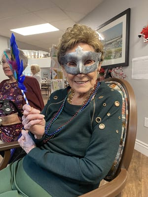 Resident enjoying a festive activity with a mask and beads