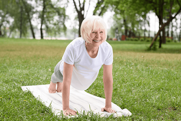 Elderly woman practicing yoga outdoors on a mat