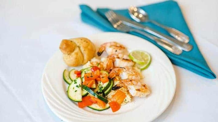 A plate of shrimp with vegetables and a bread roll
