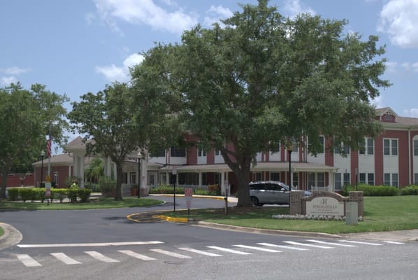 A view of the entrance and exterior of Spring Hills Hunters Creek with trees and a sign.