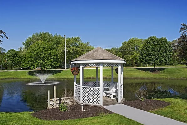 A gazebo by a pond surrounded by greenery