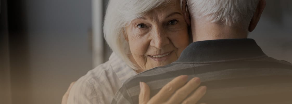 An elderly woman smiling while hugging a man