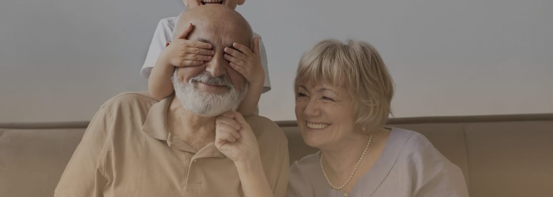Elderly couple smiling with child over their eyes