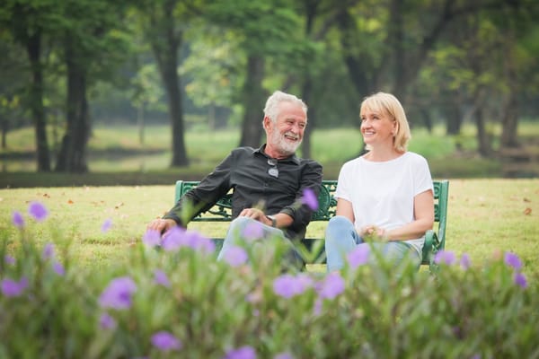A senior man and woman enjoying time together on a bench in a garden.