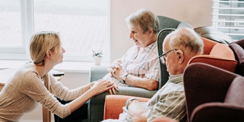 A caregiver interacting with two residents in a cozy lounge