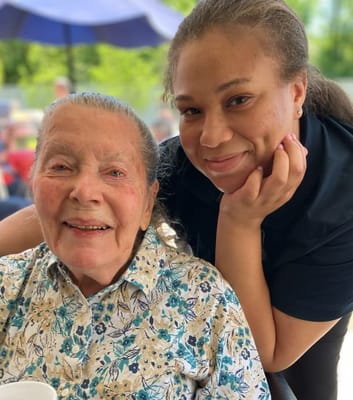A resident and staff member smiling together outdoors