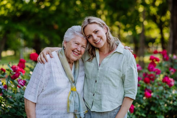 Senior resident and visitor smiling in a garden