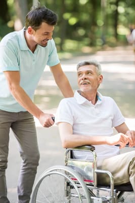 A caregiver smiling at a resident in a wheelchair outdoors