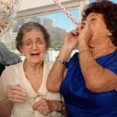 Two elderly women celebrating with balloons and party horns