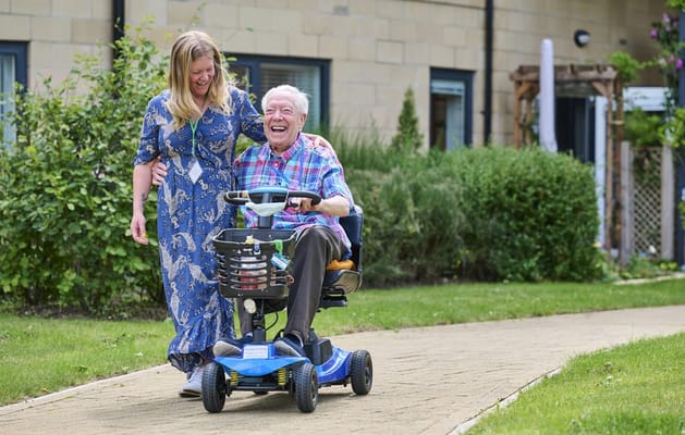 Resident laughing on a mobility scooter with staff member
