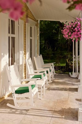 Rocking chairs on a covered porch surrounded by greenery