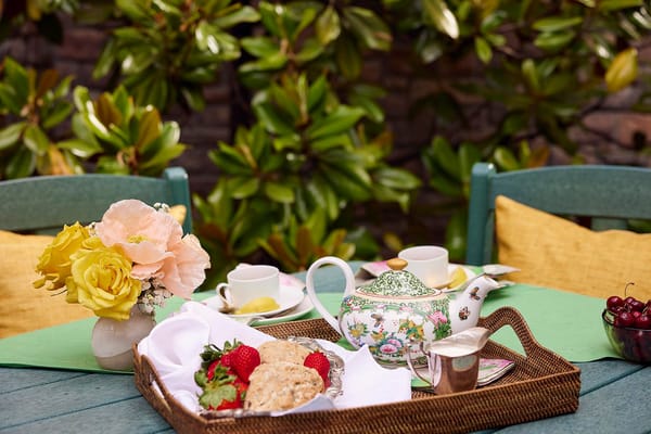 A beautifully arranged outdoor tea setting with flowers and fruits