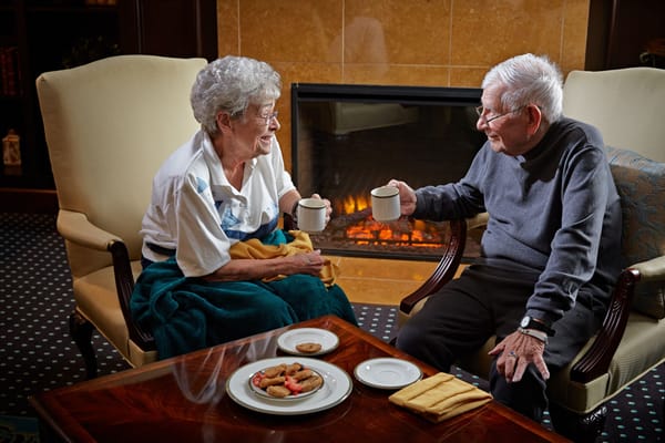 Two residents enjoying tea by a fireplace