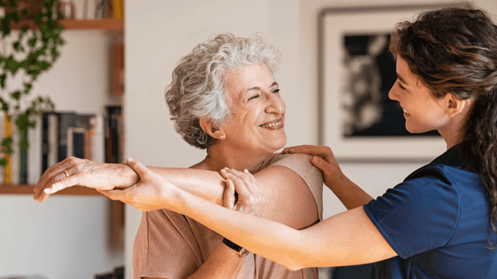 A caregiver assisting a senior woman in a bright therapy room