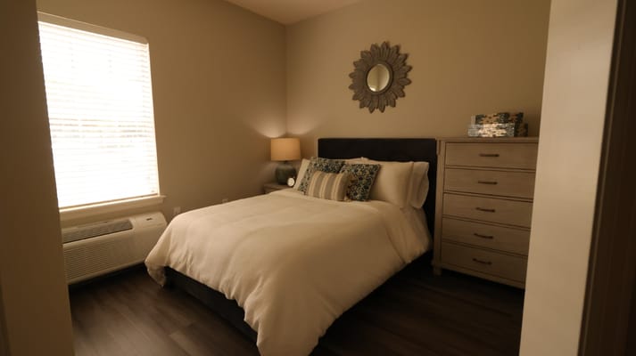 A well-furnished bedroom with a bed, lamp, and dresser.
