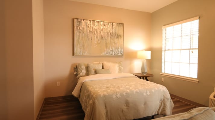 A cozy bedroom featuring a bed with decorative pillows, a bedside lamp, and a painting on the wall.