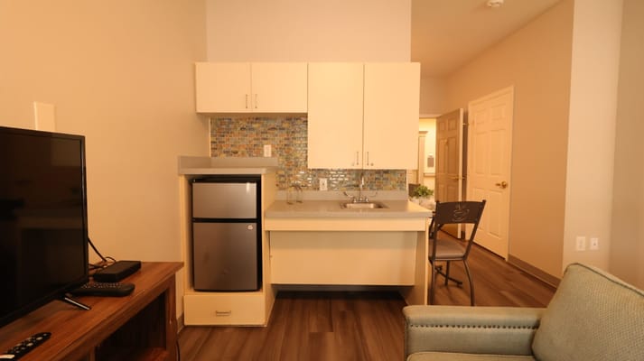 A kitchenette featuring a sink, refrigerator, and cabinets in a senior living apartment.