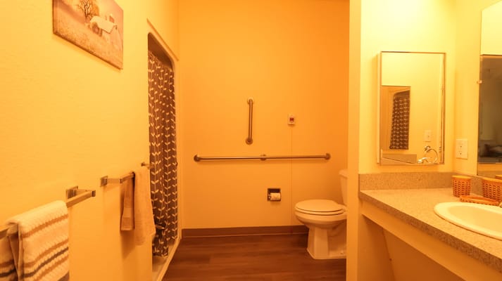 A well-lit bathroom with a shower, sink, and towels