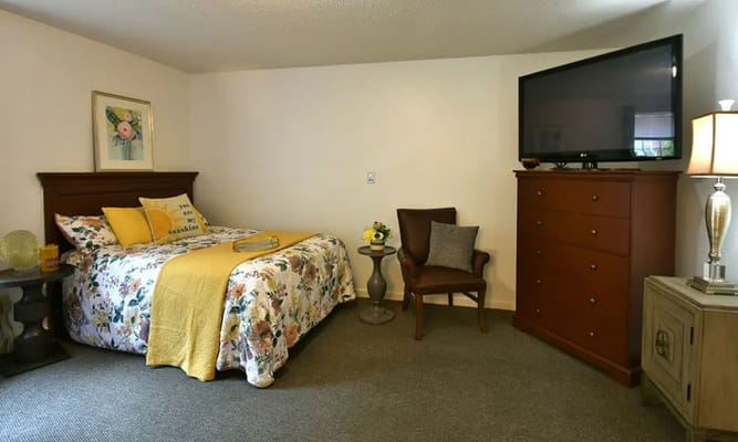 Spacious bedroom featuring floral bedding, a TV, and a comfortable chair.