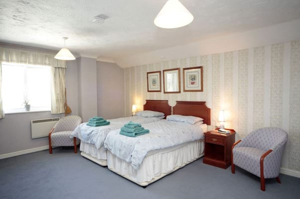 A spacious bedroom with twin beds, soft blue linens, and a cozy seating area.
