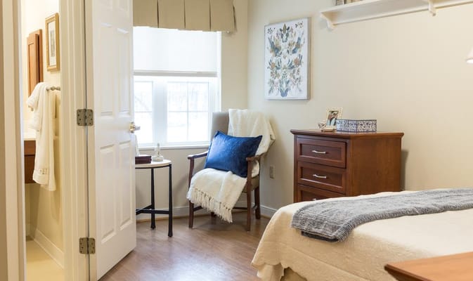 A cozy senior living bedroom with a chair, blanket, and chest of drawers.