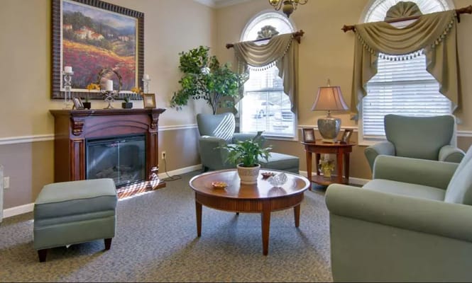 A comfortable living room with green armchairs, a round coffee table, and a fireplace.