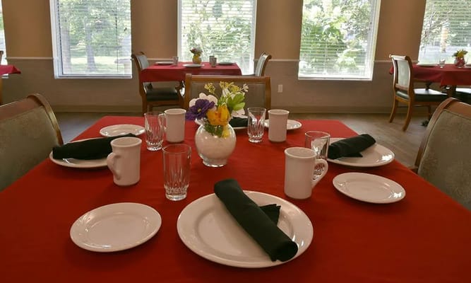 Table set for dining with red tablecloth, plates, glasses, and flower centerpiece.