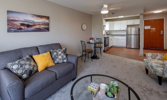 Living room area with a sofa, dining table, and kitchen in the background.