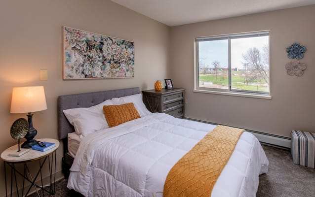 A cozy bedroom with a queen bed, lamp, and window view.