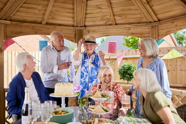 Seniors celebrating with food and laughter under a gazebo.