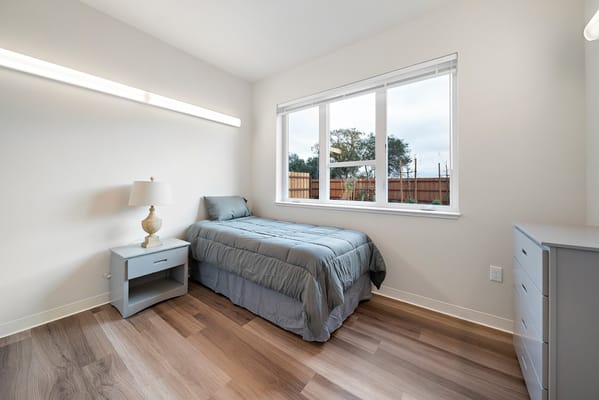 A cozy bedroom with a single bed, lamp, and large window