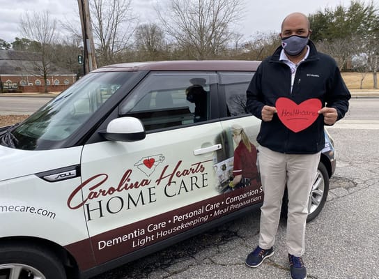 Person holding a heart sign next to a branded vehicle