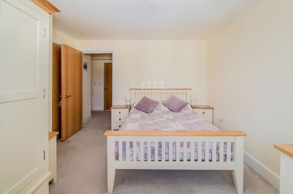 A neatly arranged bedroom with a double bed and light-colored furniture.