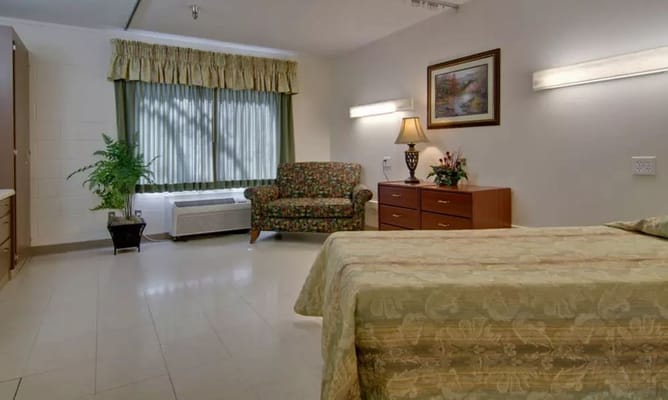 Comfortable room featuring a bed, chair, and dresser with window view.