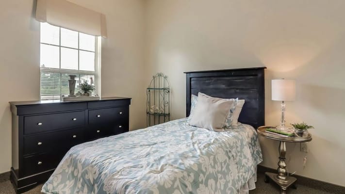 A cozy bedroom with a bed, dresser, and lamp.